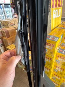 Damaged door seal on a commercial fridge showing cracks and gaps, leading to cold air loss and reduced efficiency.