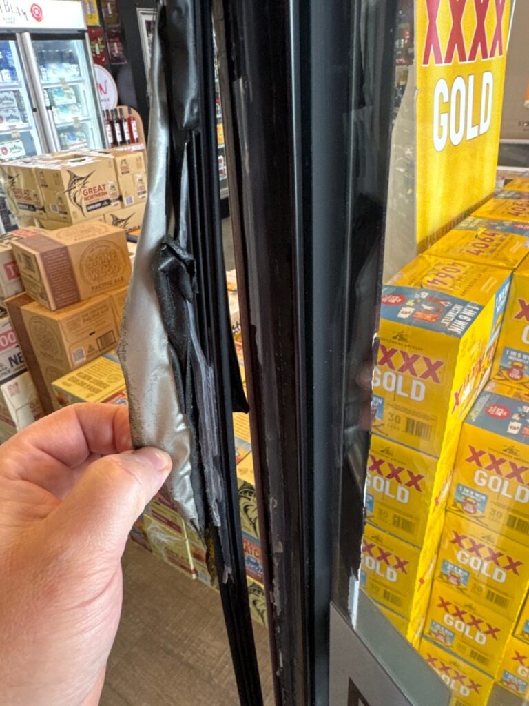 Damaged door seal on a commercial fridge showing cracks and gaps, leading to cold air loss and reduced efficiency.